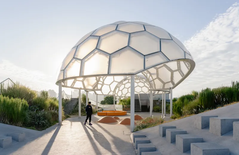 Hexagonal dome pavilion with translucent panels and structural frame casting long shadows at sunset