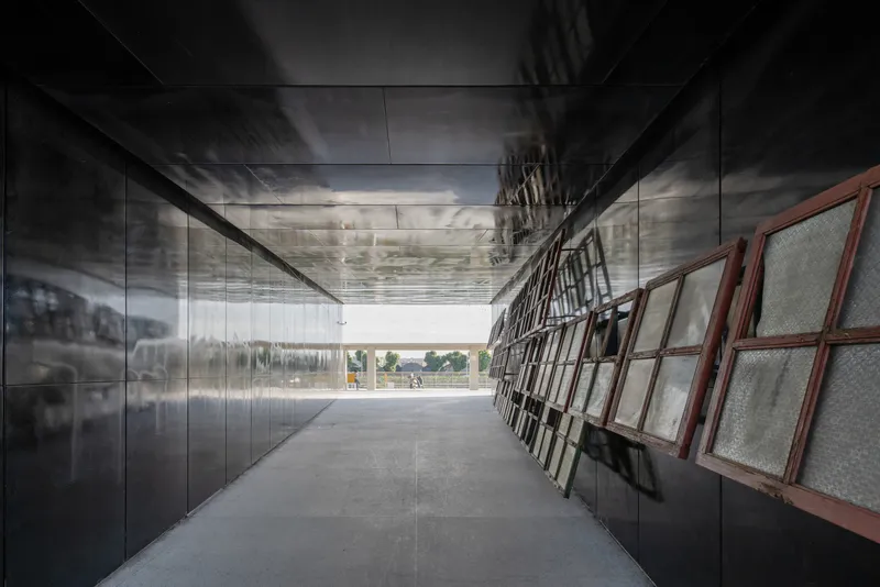 Corridor with reflective metal wall panels and angled wire mesh screens under a polished ceiling