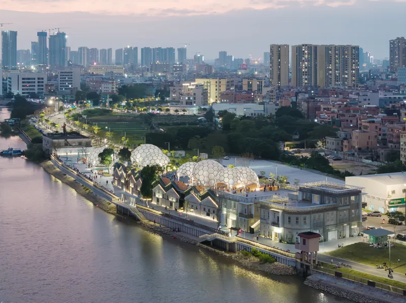Aerial view of the riverside complex with illuminated geodesic domes at dusk against the urban skyline