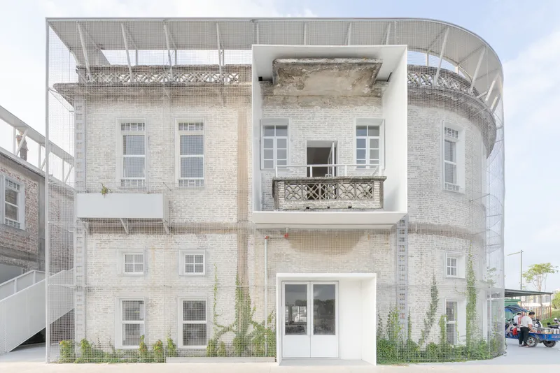 Preserved brick facade enclosed by a new white structural frame with mesh balustrades and climbing vegetation