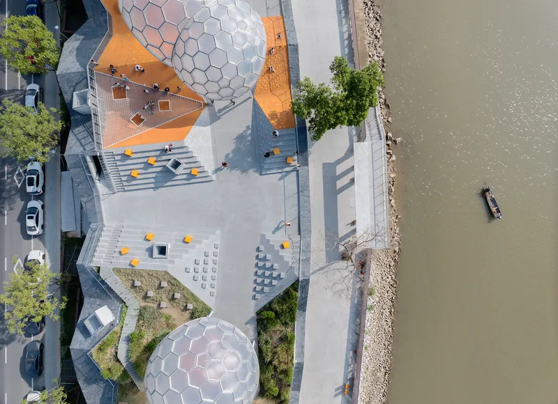 Aerial view of the waterfront plaza with hexagonal dome structures and a boat passing in the river