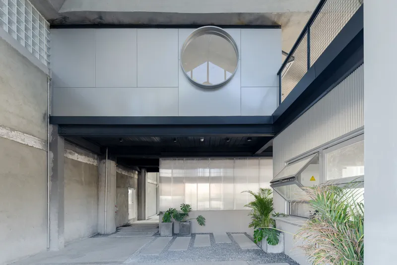 Covered courtyard entrance with circular portal window, exposed concrete columns, and potted plants on gravel