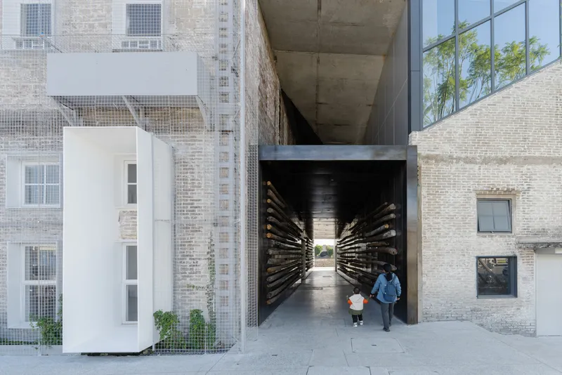 Pedestrian passage through brick buildings with radial timber slat walls and an adult walking with a child