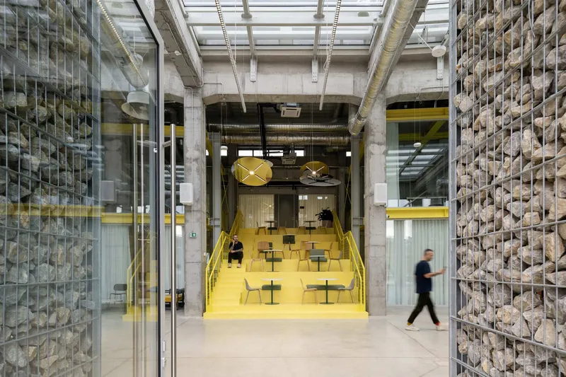 Interior corridor with yellow tiered seating flanked by gabion walls and exposed concrete columns
