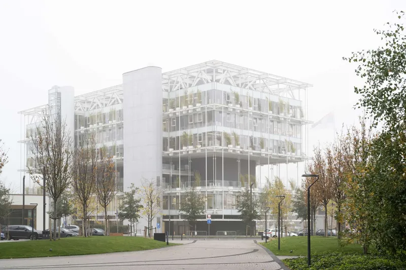 Glass and steel facade with exposed white truss structure viewed from the street on an overcast autumn day