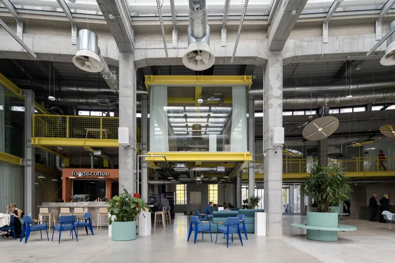 Ground floor lobby space with concrete structure, yellow metal railings and planted seating areas