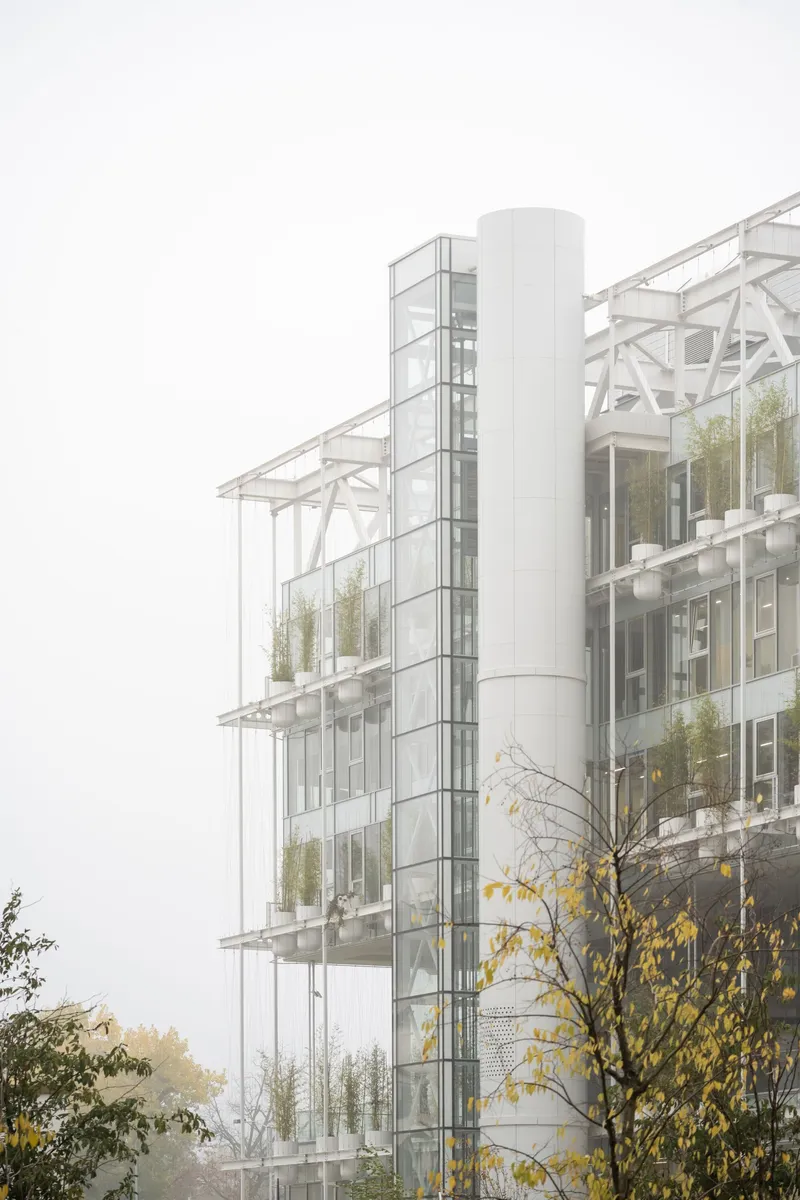 Glass facade with white steel truss canopy and planted terraces visible through heavy fog