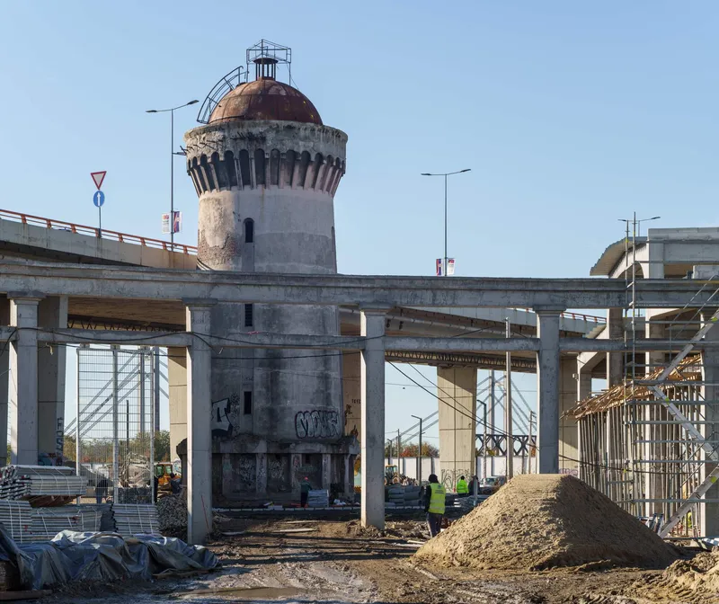 Weathered cylindrical tower with copper dome surrounded by construction site and concrete frame structure