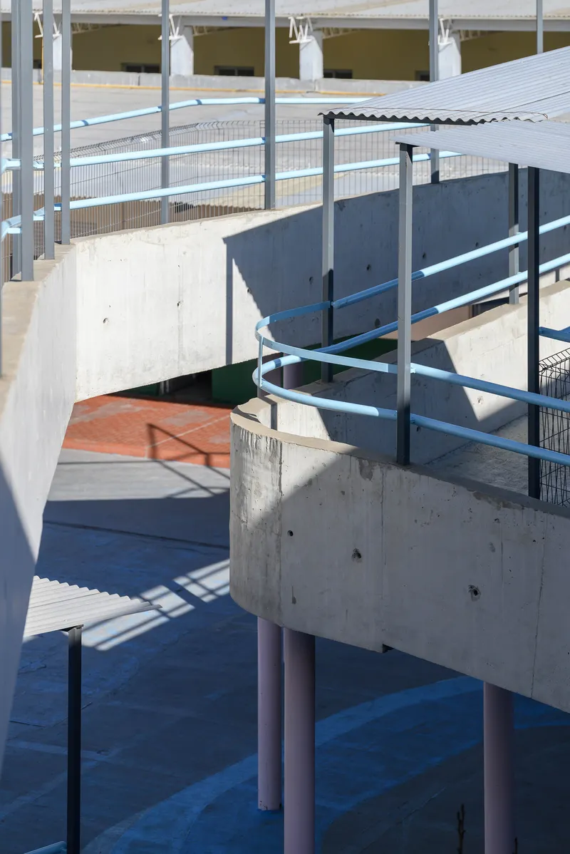 Close-up of concrete platforms with pink tubular columns and blue metal railings casting sharp shadows