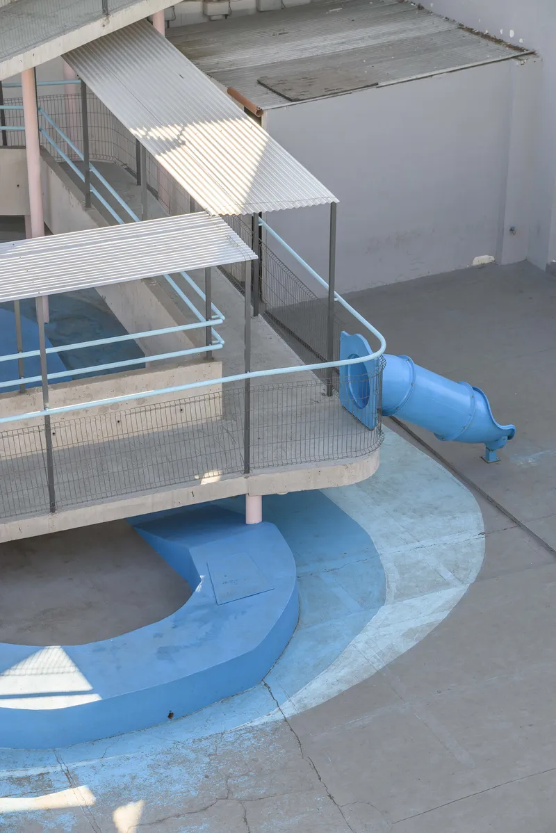 Top-down view of blue slide curves descending from wire mesh-enclosed platform with corrugated metal shelter