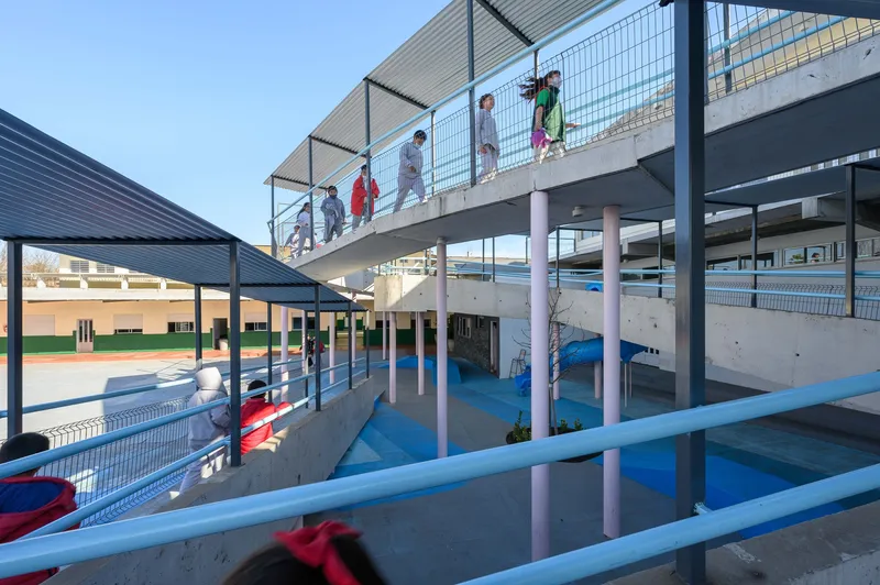 View of stacked concrete ramps and blue slide beneath a metal canopy with children ascending the upper level