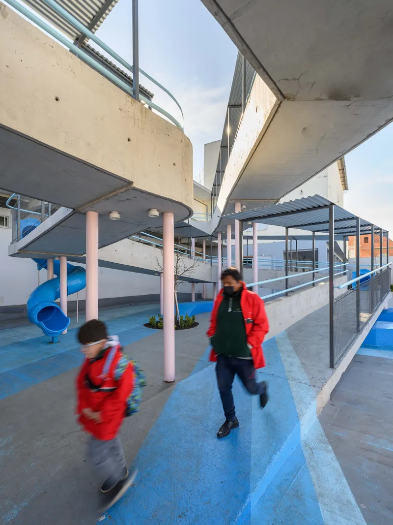 Overlapping concrete decks supported by pink cylindrical columns with students in motion beneath angular overhangs