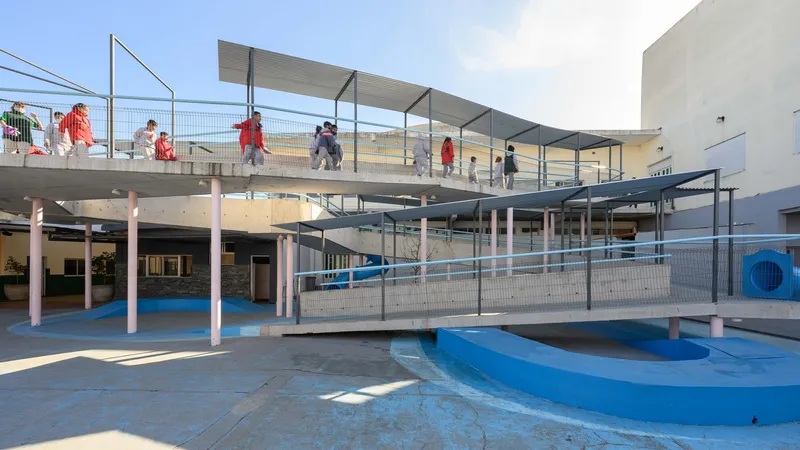 Elevated concrete ramps and walkways with wire mesh railings over a blue painted courtyard with students crossing