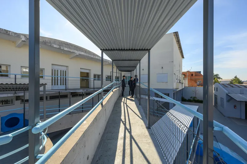 Long covered concrete walkway with corrugated metal canopy creating shadow patterns on the ground as people walk
