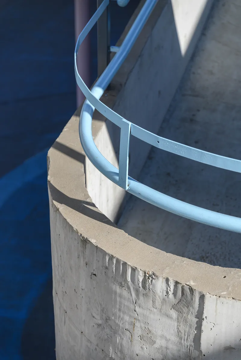 Detail of curved blue metal railing wrapping the edge of a cast concrete planter in sunlight