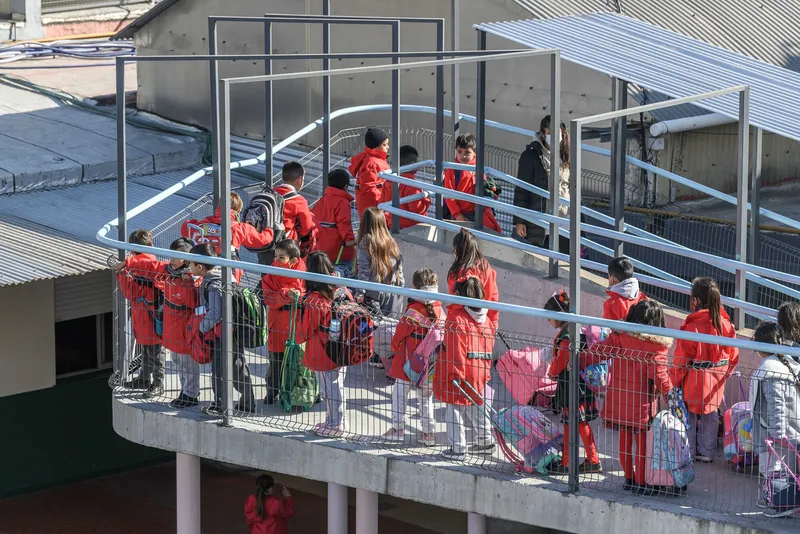 Elevated concrete walkway with students in red jackets gathered along blue and wire mesh railings