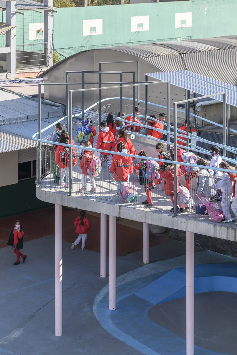Curved concrete ramp on pink columns filled with students in red jackets descending to the courtyard