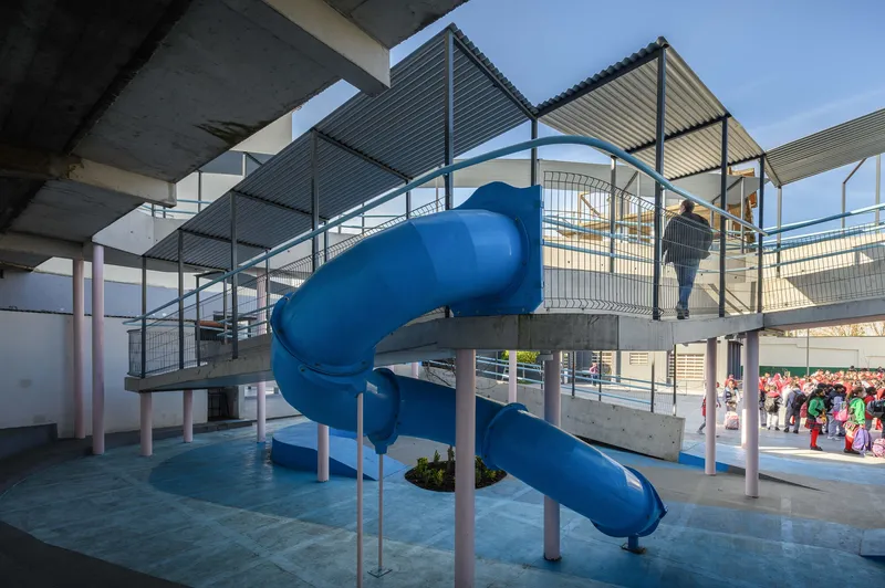 Blue spiral slide emerging from an elevated platform with metal mesh railings and concrete roof canopies