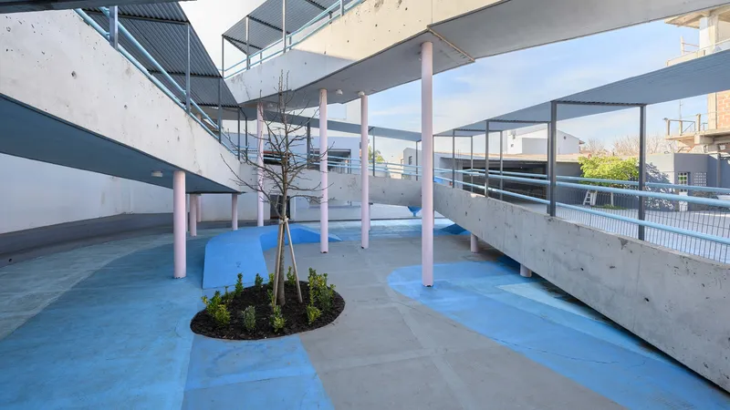 Courtyard with a circular planting bed, pink columns, blue paving, and concrete ramps under open sky