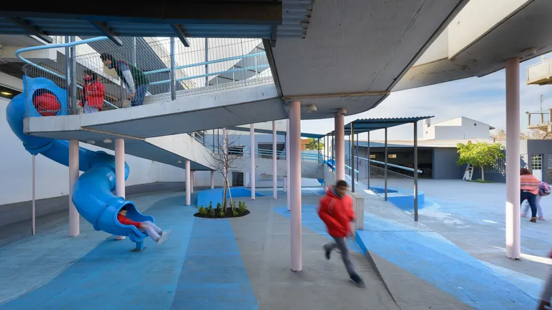 Blue slide and pink columns with children moving through the courtyard under corrugated metal canopies