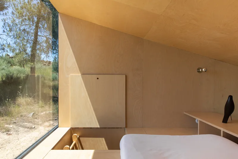 Plywood bathroom with corner glazing framing dry summer grasses and a freestanding white bathtub