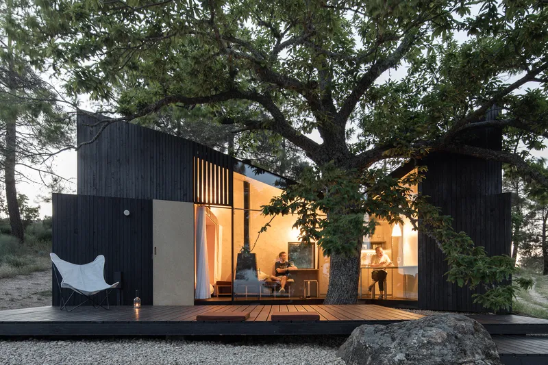 Timber deck extending from glass-walled living space with two people seated inside at twilight