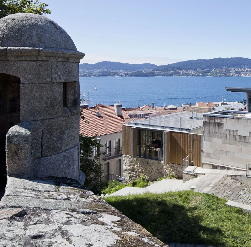 View past a granite turret down toward timber-screened balconies with bay and hillside in the distance