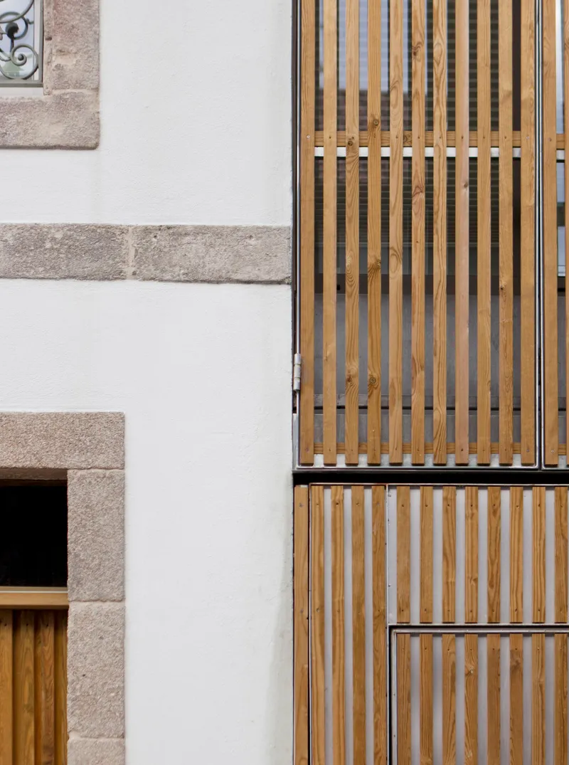 Detail of vertical timber slat screens against white stucco wall with granite quoins at window opening