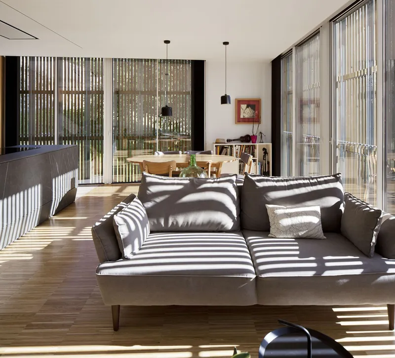 Open-plan living space with vertical timber screens filtering sunlight into geometric shadow patterns