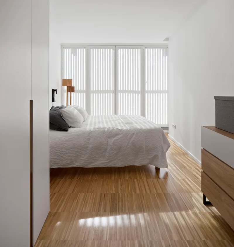 Bedroom view through a timber-framed doorway with vertical blinds casting striped shadows on the floor
