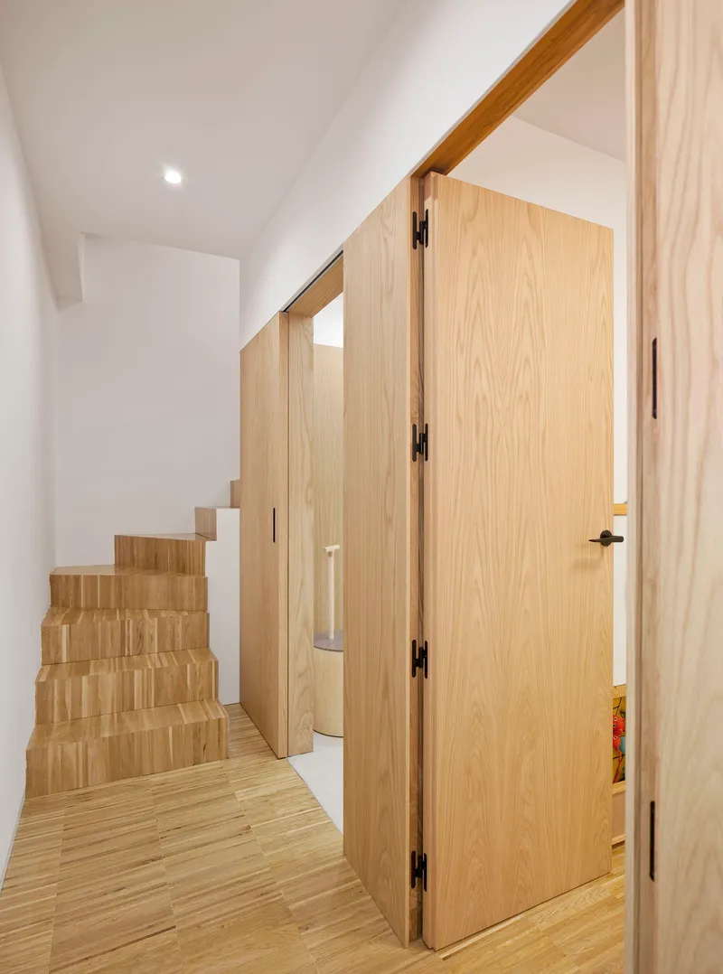 Light oak staircase and flush door beneath a sloped ceiling in a narrow corridor