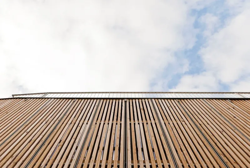 Upward view of vertical timber slat facade against a cloudy sky