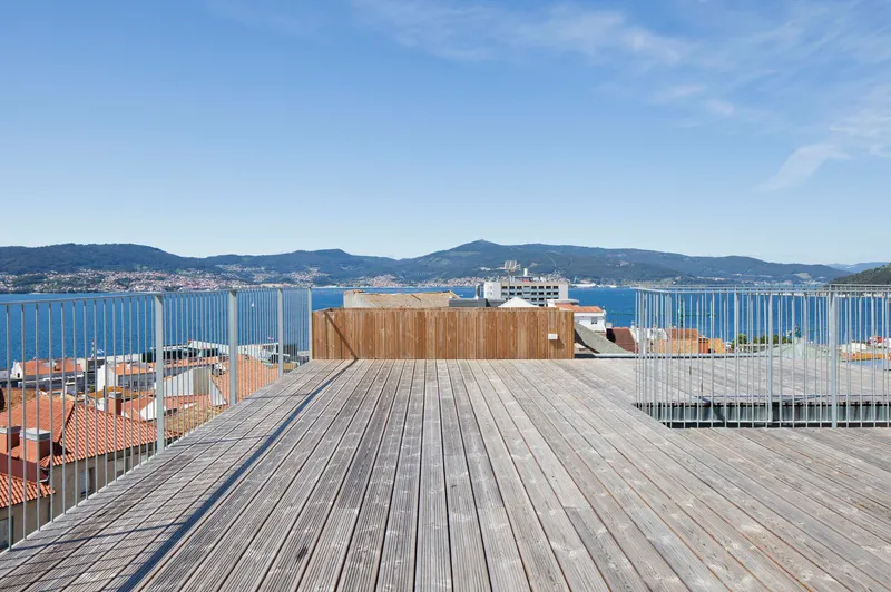Rooftop timber deck with vertical slat railing overlooking a bay and distant hills