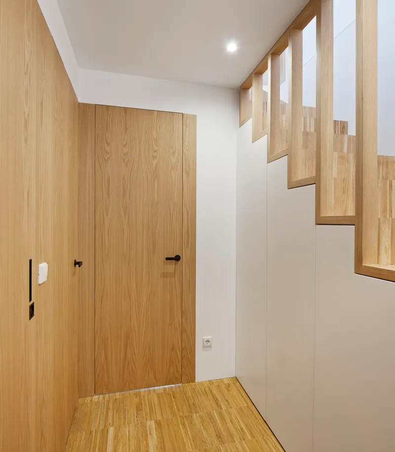 Entry vestibule with oak-clad door and open-tread staircase ascending along the wall