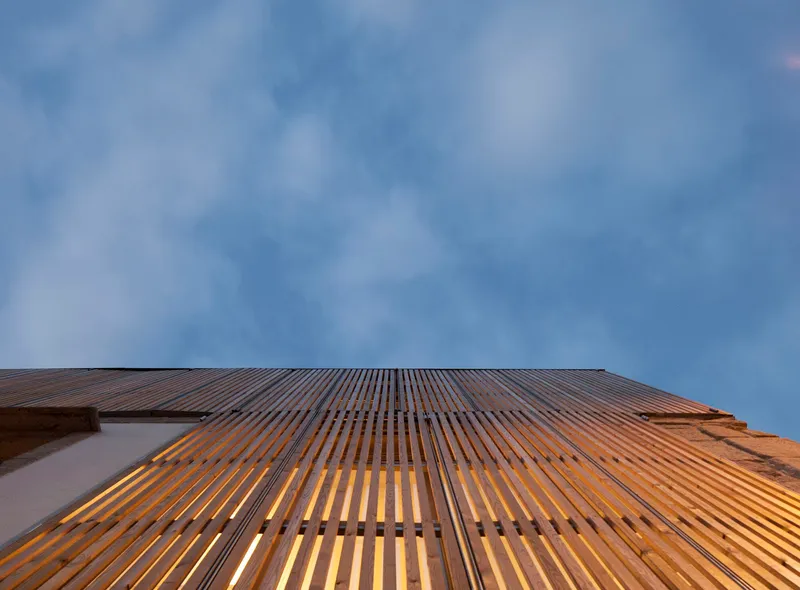 Timber slat screen facade illuminated from within at dusk beneath stormy clouds