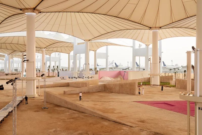 Covered outdoor plaza with radial fabric canopies supported by white columns with aircraft visible beyond