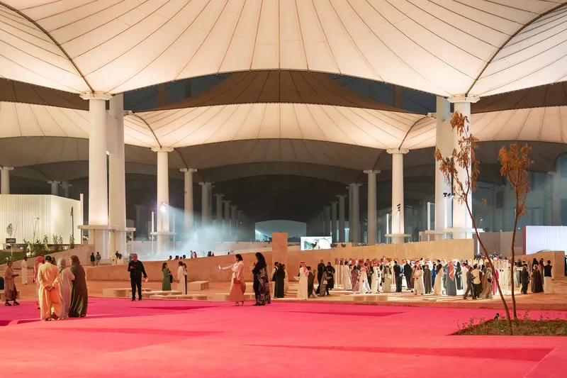 Gathering of people on a pink carpet runner beneath the radial canopy structure at dusk