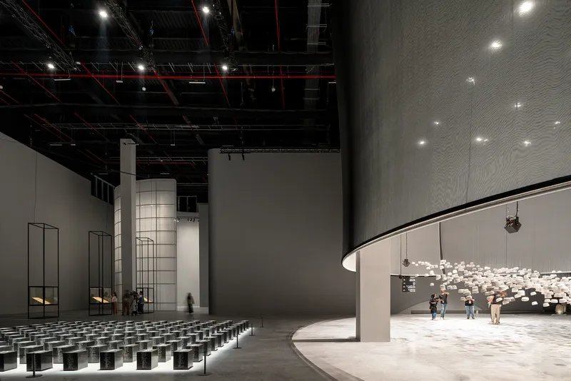 Interior auditorium with curved balcony, exposed black ceiling infrastructure, and rows of dark seating cubes