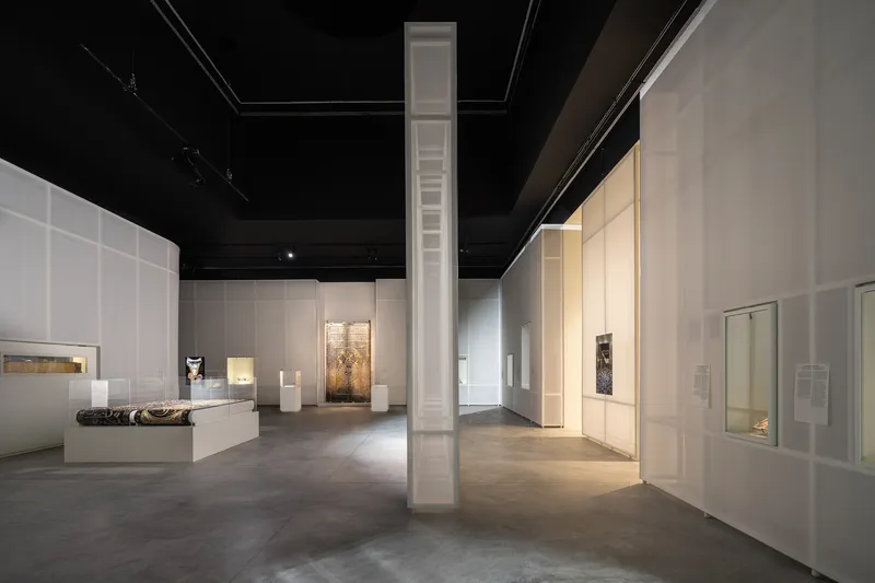 Gallery space with white partition walls, black ceiling, and tall white column beneath track lighting