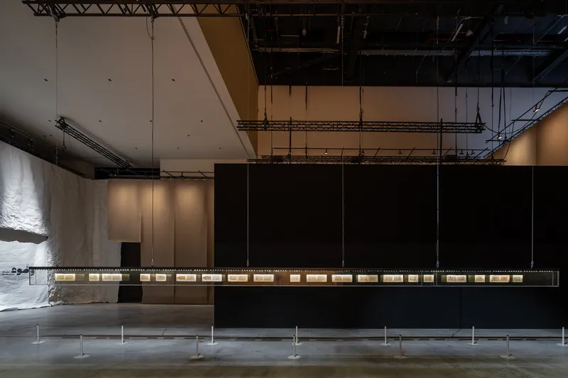 Long horizontal display case suspended below exposed structural trusses and black partition wall