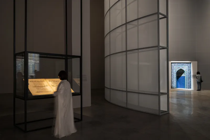 Gallery interior with translucent wall panels and illuminated display cases viewed by a visitor in white