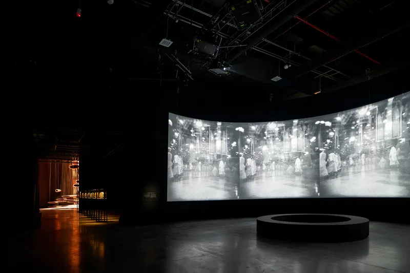 Curved projection screen displaying archival imagery above a circular platform in a darkened exhibition space