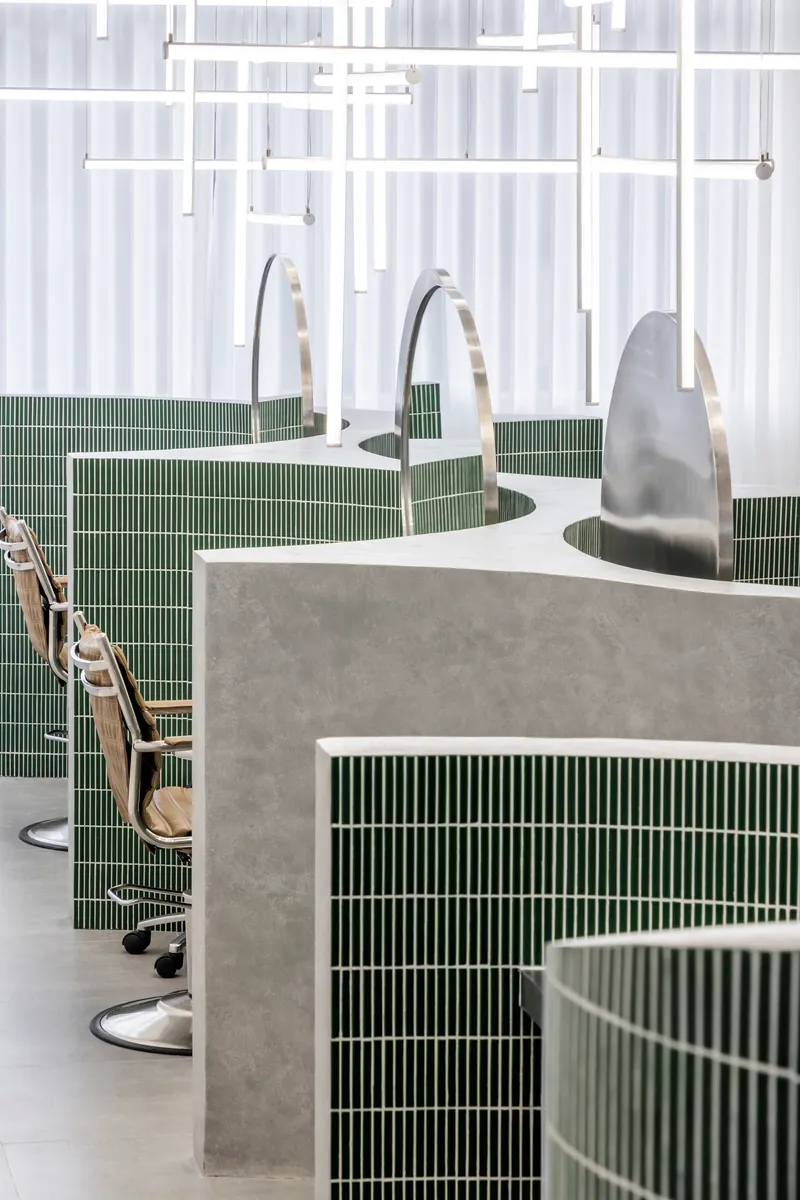 Salon stations with curved concrete and green tile bases beneath white translucent curtain dividers