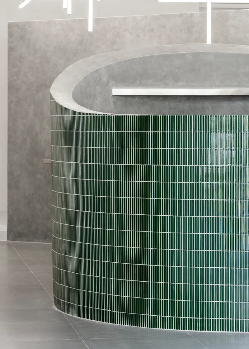 Curved counter clad in vertical green ceramic tiles beneath a concrete soffit