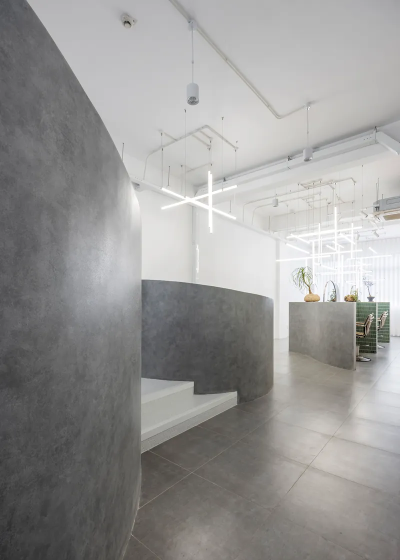 Curved concrete reception desk with built-in bench seating beneath exposed white ceiling and linear lighting