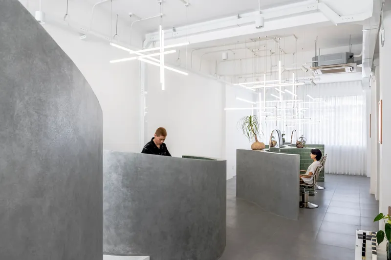 Reception area with curved concrete desk under suspended white linear lighting grid and sheer curtains
