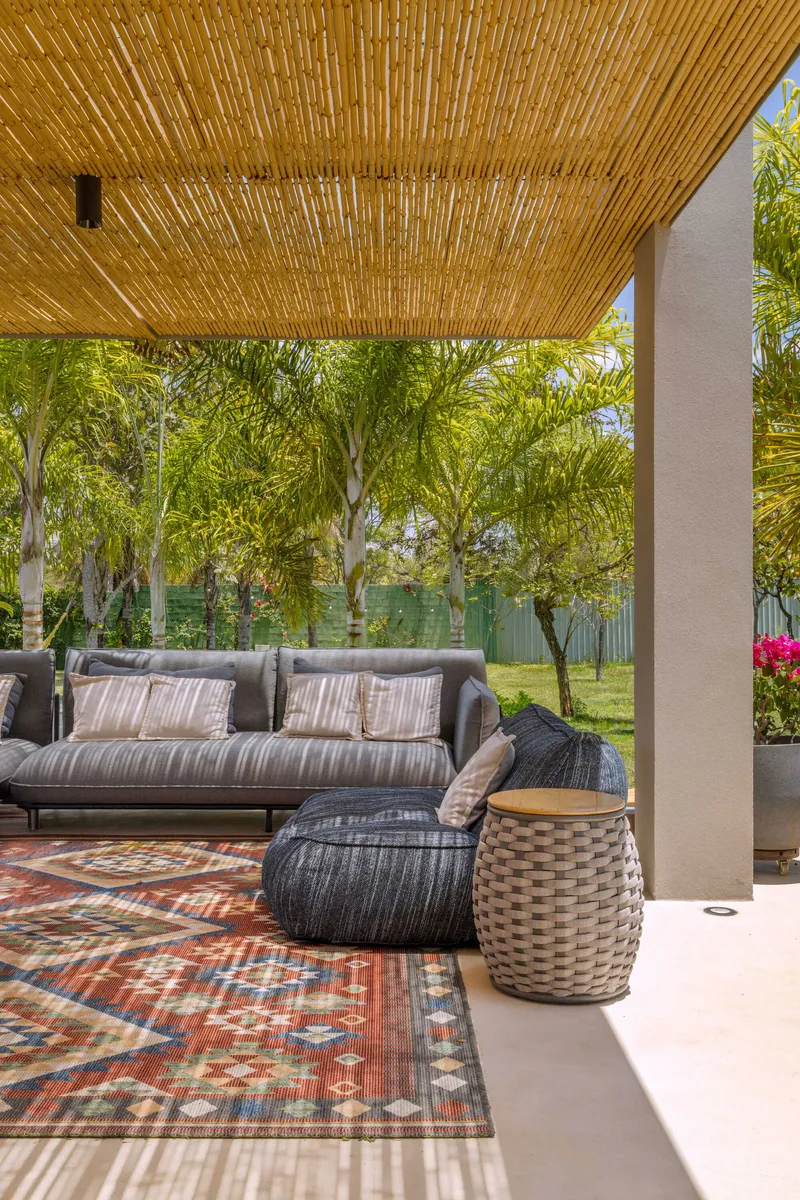 Covered terrace with bamboo slat ceiling and woven outdoor furniture overlooking a lawn and trees