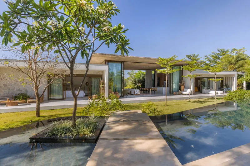 Concrete walkway crossing a reflecting pool flanked by planted beds and young trees