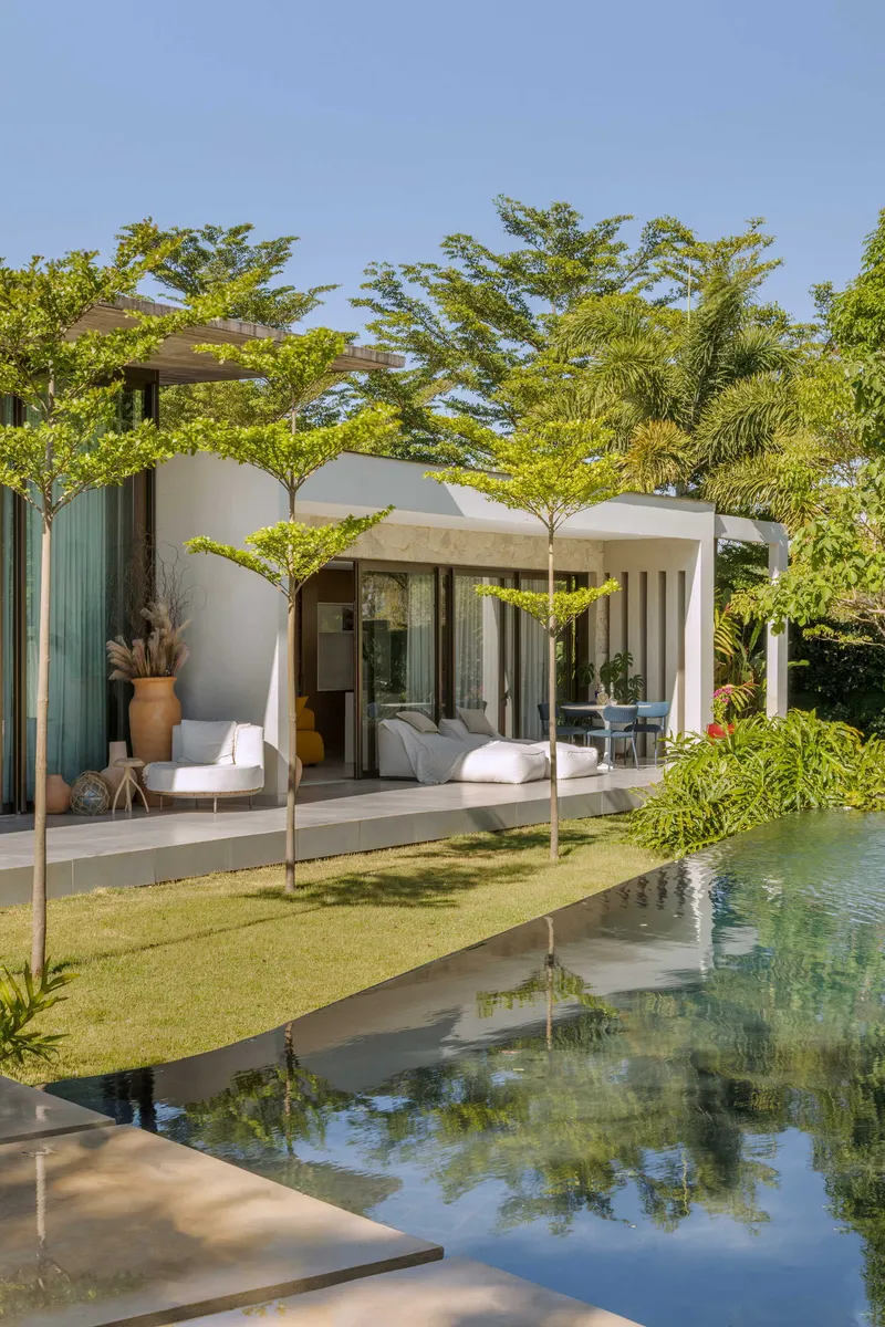 Curved white wall enclosing a covered patio beside a still pool and scattered trees