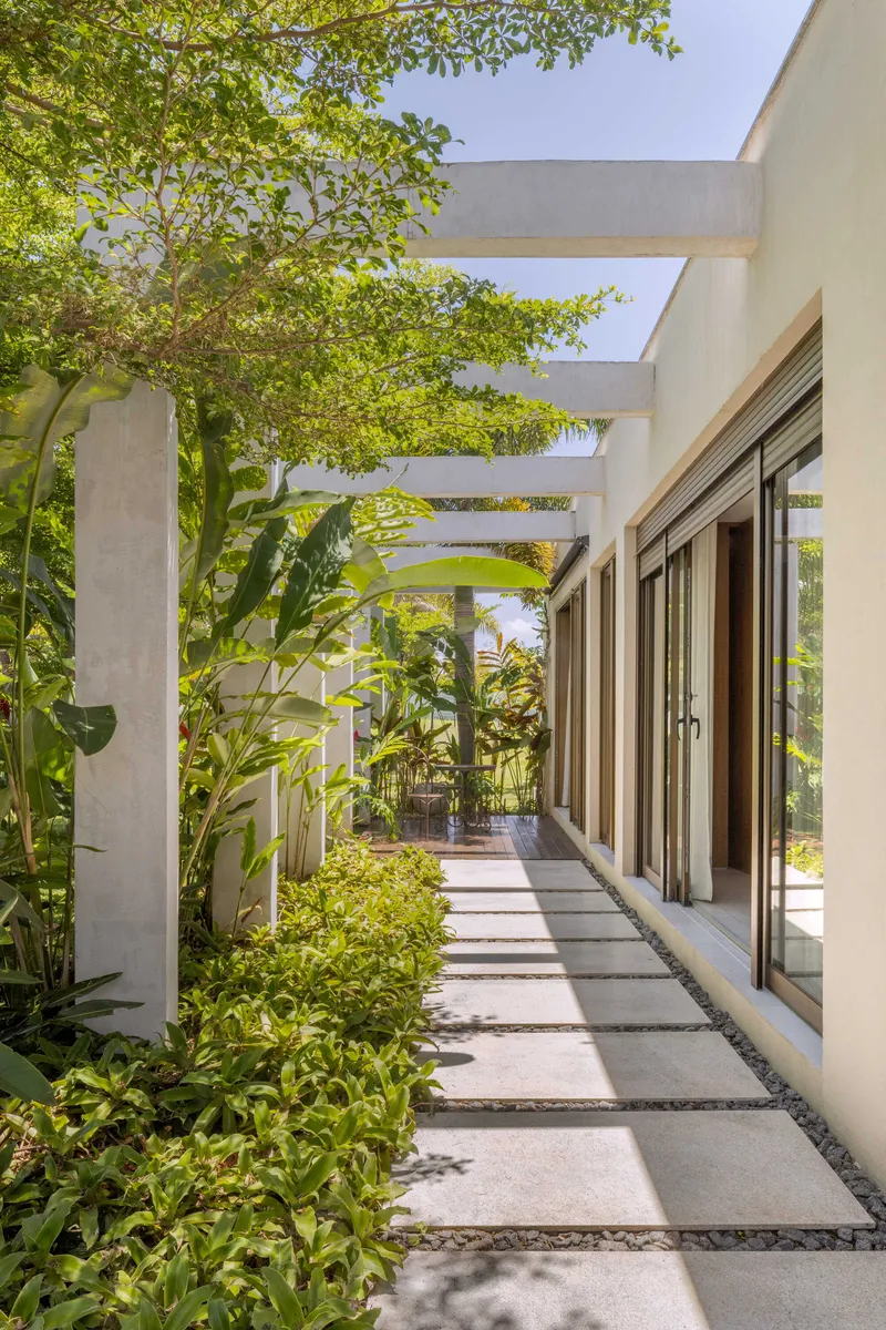 Side walkway with paving stones, gravel edging and concrete pergola shaded by overhanging tree